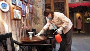 Una persona limpiando una mesa de madera en una habitación con paredes de piedra y cuadros enmarcados.