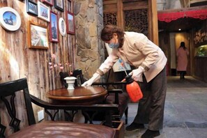 Una persona limpiando una mesa de madera en una habitación con paredes de piedra y cuadros enmarcados.