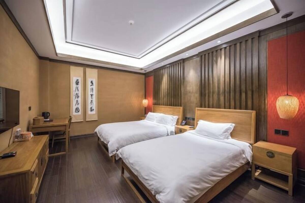 A hotel room with two beds, a desk, a TV, and a wall with vertical wooden panels.