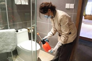Una persona limpiando un inodoro en un baño con mampara de vidrio.