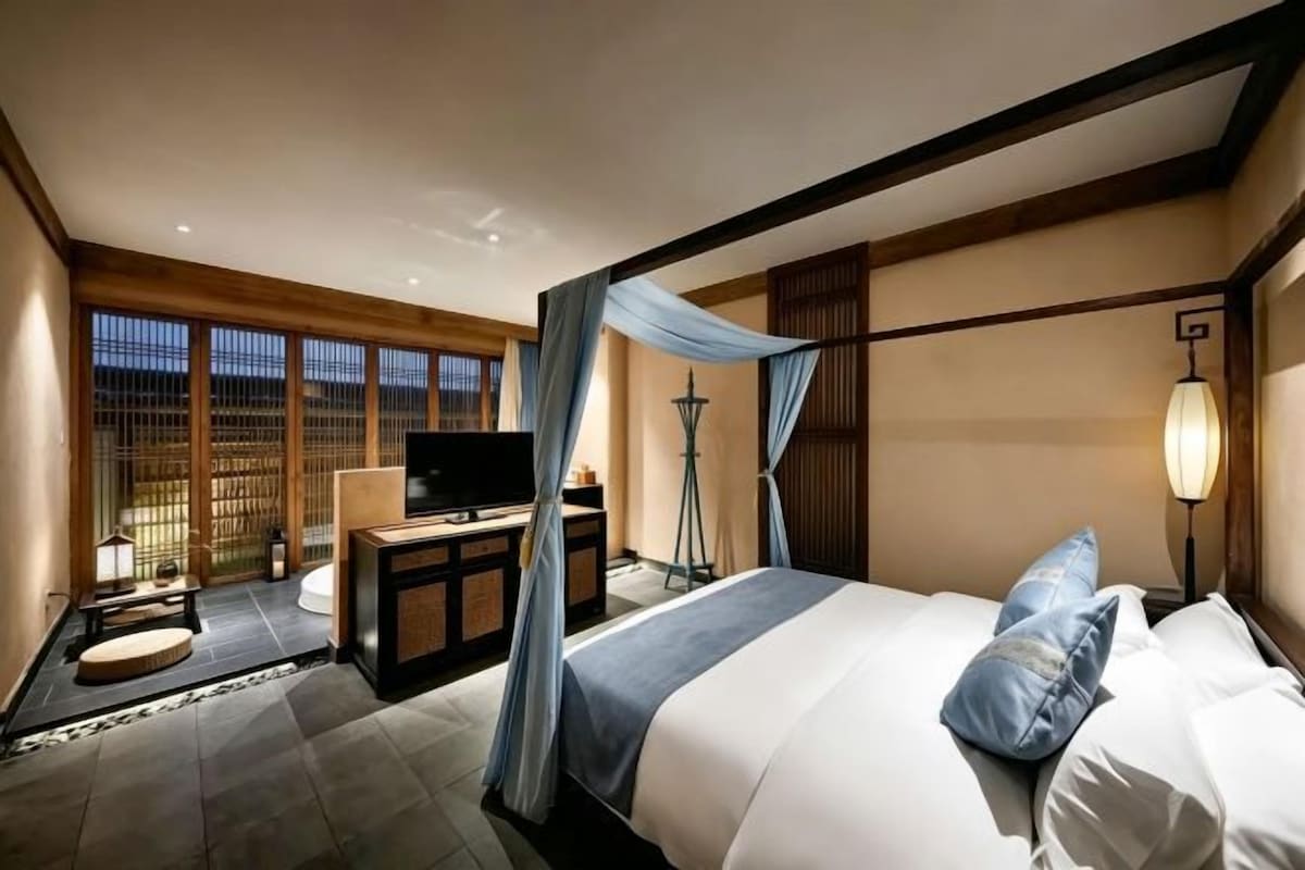 Une chambre d’hôtel avec un lit, un bureau avec une télévision, une lampe sur pied et une fenêtre donnant sur un beau paysage.