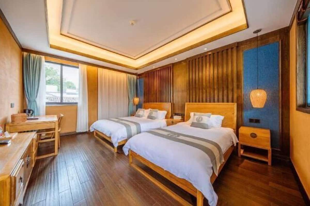 A hotel room with two beds, a desk, and a window.
