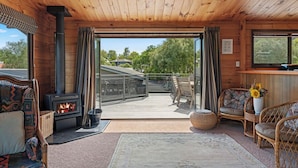 Interior acogedor de una cabaña con estufa de leña, mobiliario de mimbre y vistas al exterior.
