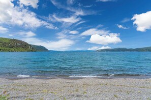 A calm lake with a pebble beach and distant hills.