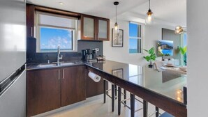 A modern kitchen with dark wood cabinets, a stainless steel refrigerator, and a large window offering a view of the sky. - BeachFront Haven/Isla Verde Prime Location/Parking (Carolina)