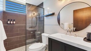 A modern bathroom with a glass-enclosed shower, a white toilet, a large round mirror, and a white sink with a black countertop. - BeachFront Haven/Isla Verde Prime Location/Parking (Carolina)