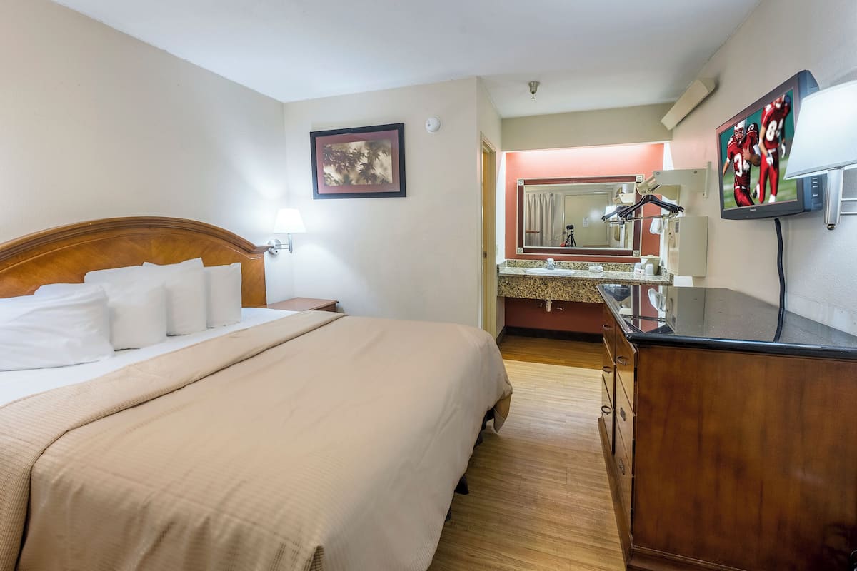 A hotel room with a bed, a wooden dresser, a television, and a bathroom visible in the background.