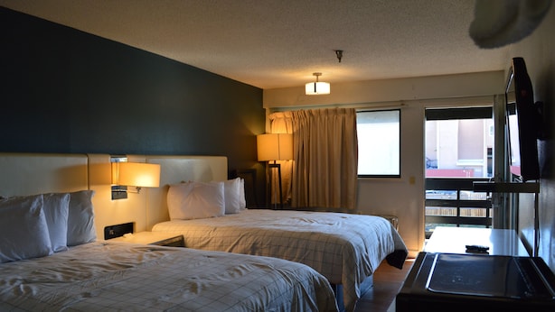 A hotel room with two beds, a desk, a TV, and a window with curtains. - BAY INN (Tampa)