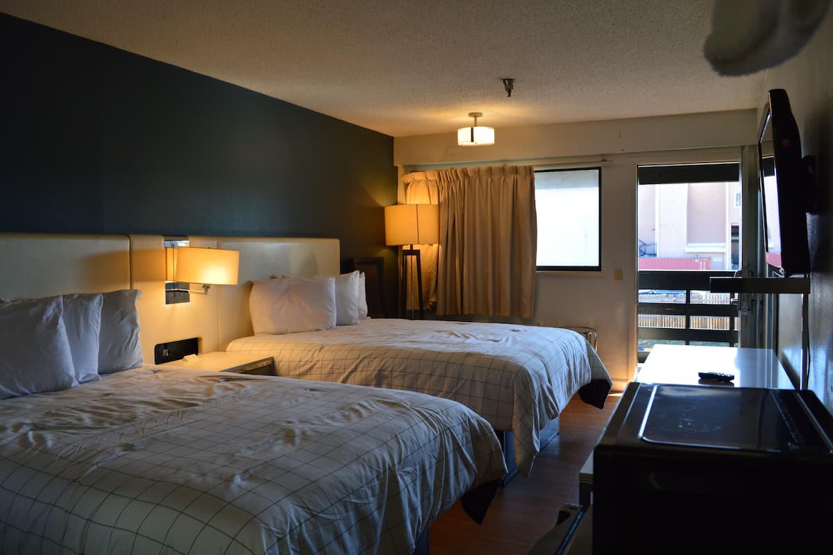 A hotel room with two beds, a desk, a TV, and a window with curtains.