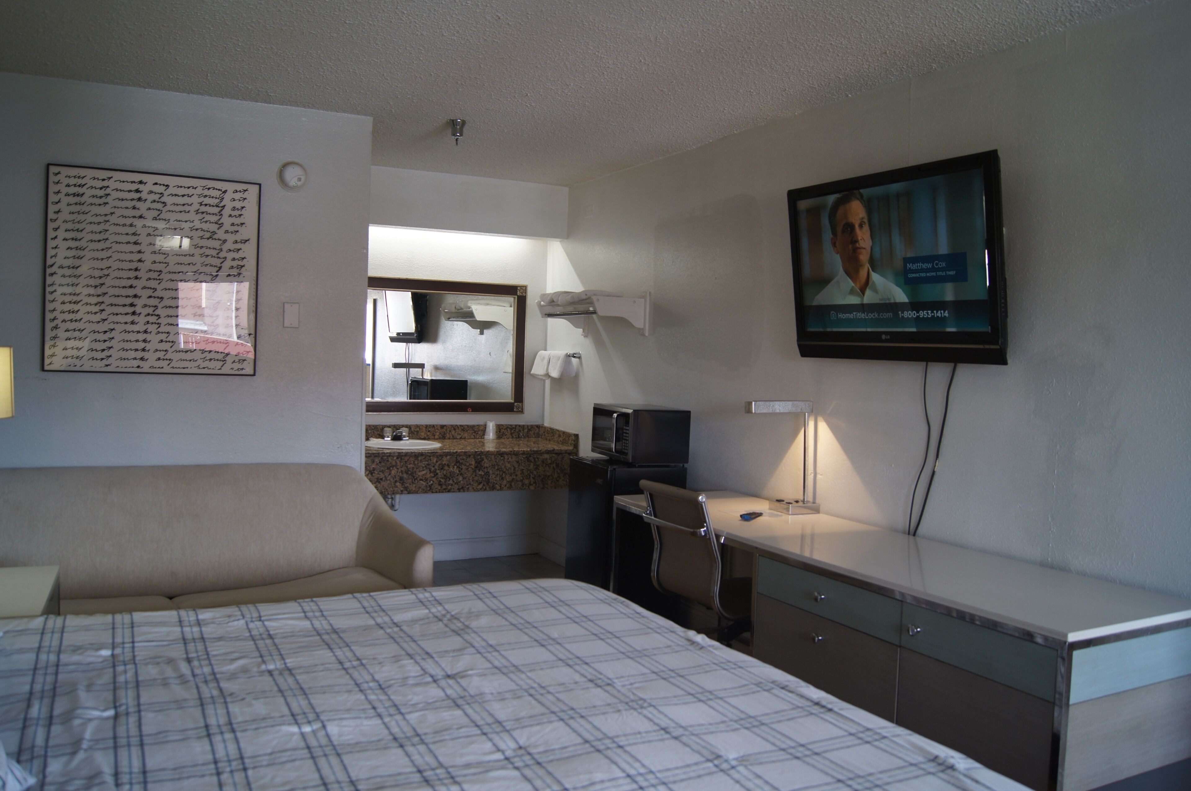 Ein Hotelzimmer mit Bett, Schreibtisch, Fernseher, einem Badezimmerspiegel und einem Wandbild.