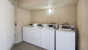 A laundry room with three stacked washers and dryers, a small window, and a ceiling light. - BAY INN (Tampa)