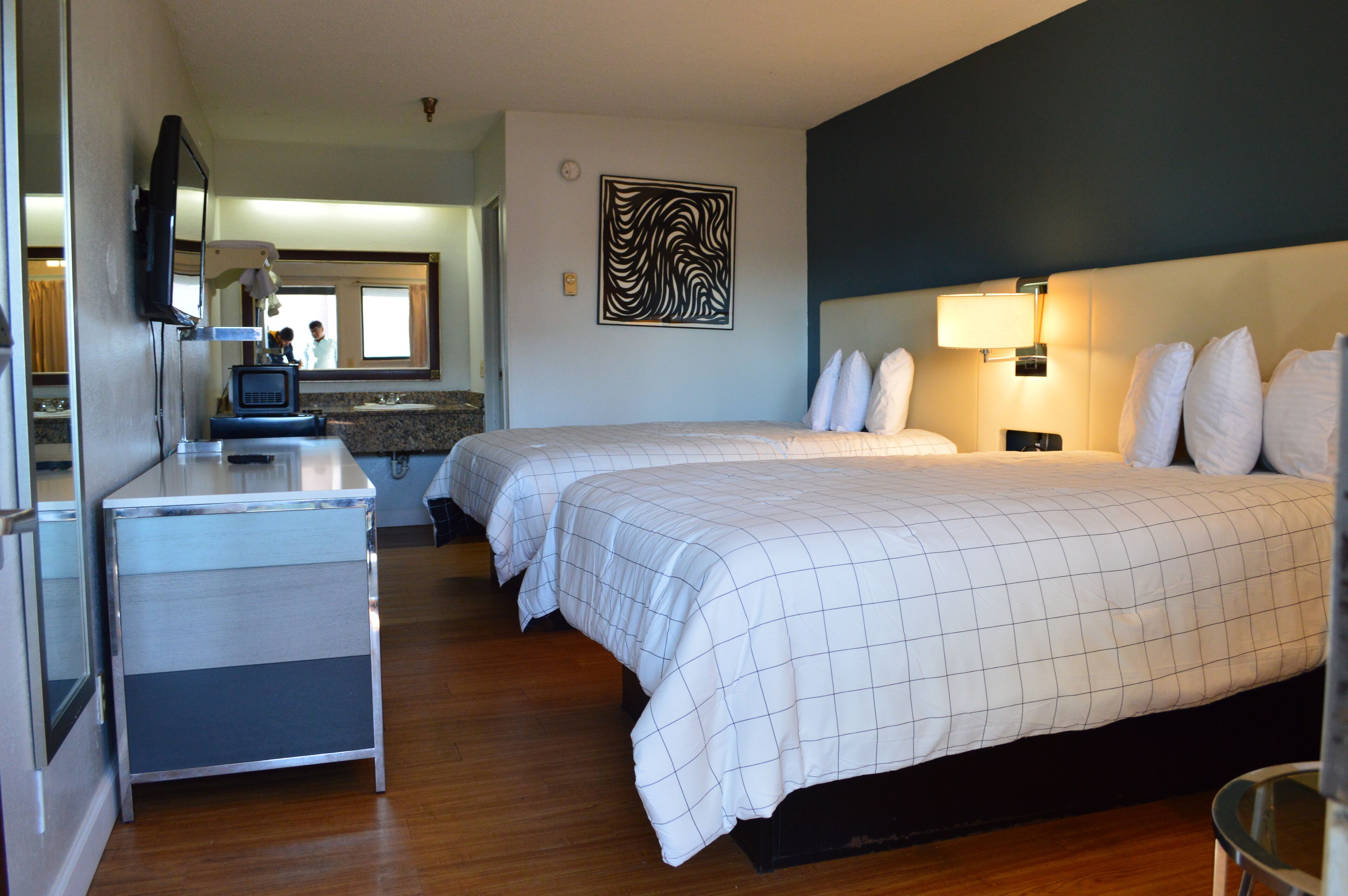A hotel room with two beds, a desk with a mirror, a television, and a bathroom visible through an open door.