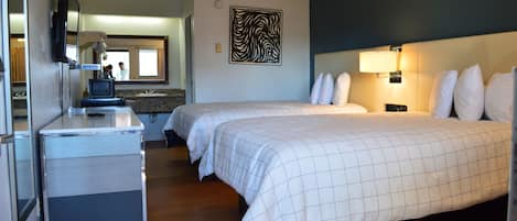 A hotel room with two beds, a desk with a mirror, a television, and a bathroom visible through an open door.