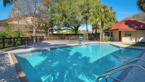 A swimming pool with a wooden deck, surrounded by trees and a fence. - BAY INN (Tampa)