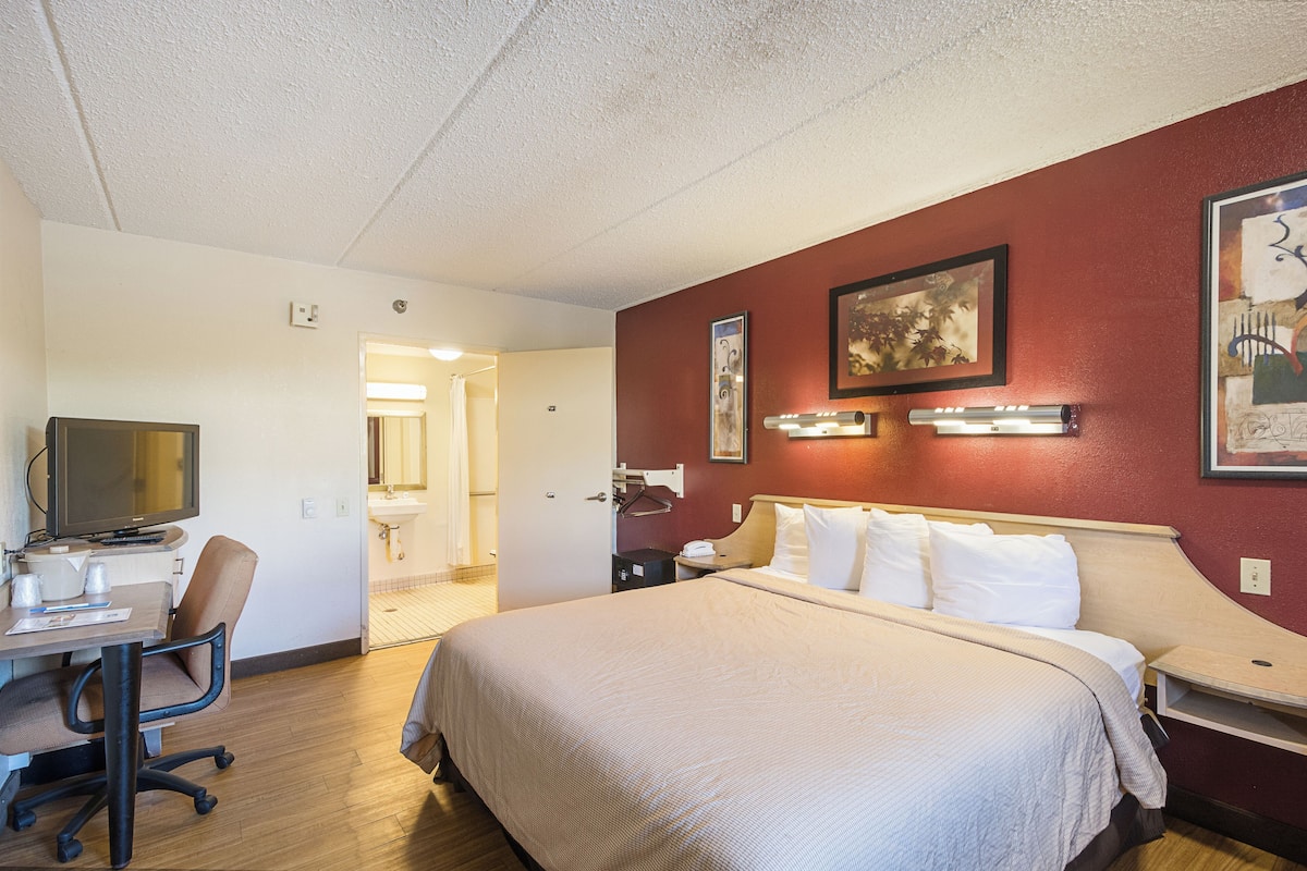 A hotel room with a bed, desk, chair, television, and artwork on the walls.