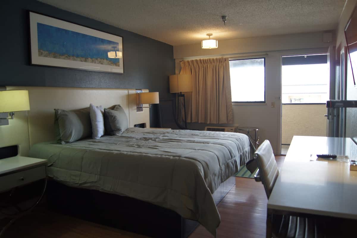 A hotel room with a bed, bedside tables, a desk, a chair, a lamp, a painting on the wall, and a window with curtains.