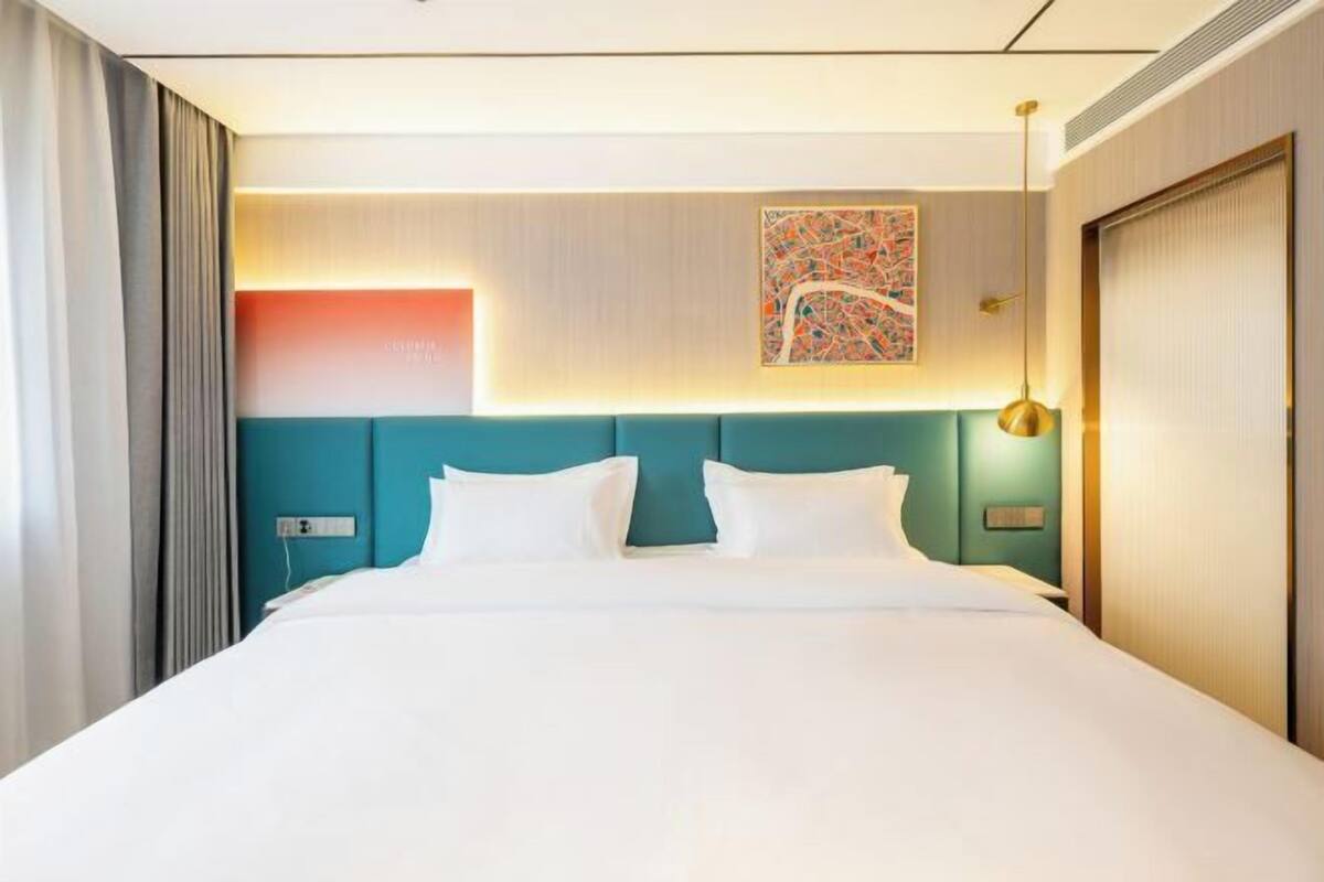 Una habitación de hotel con una cama grande, un cabecero color turquesa, una obra de arte colgada en la pared y una mesita de noche con una lámpara.