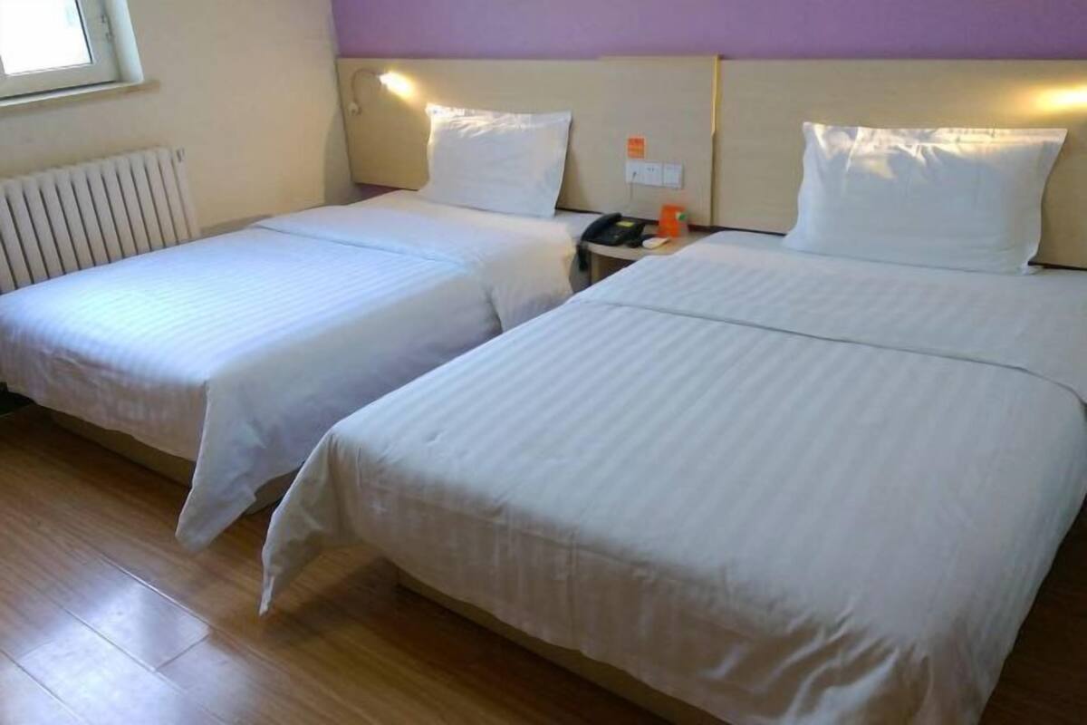 Una habitación de hotel con dos camas, una mesita de noche, un teléfono y una ventana.