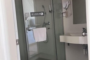 Un baño moderno con cabina de ducha de vidrio, un lavamanos blanco y una toalla colgada en un perchero.