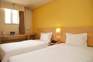 Une chambre d’hôtel avec deux lits, un bureau, une bouilloire, un téléphone et une lampe.