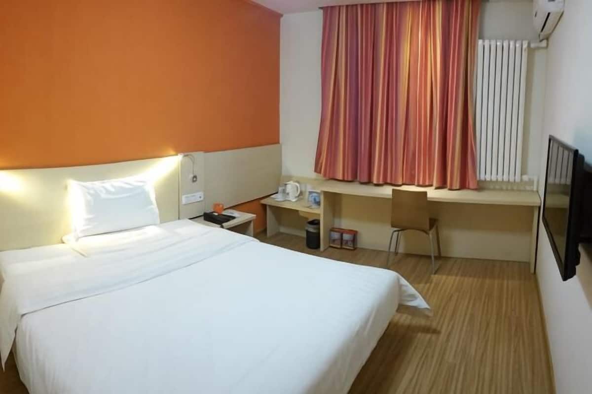 Habitación de hotel con cama, escritorio, silla, mesita de noche y ventana con cortinas.