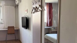 A hotel room with a bed, a desk with a chair, a TV, and a radiator.