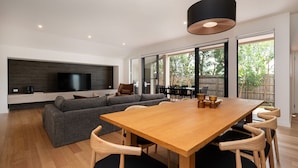 A modern living room with a large sofa, a wooden dining table, and a TV mounted on a dark wall.