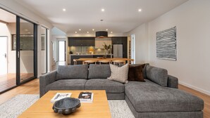 A modern living room with a grey sectional sofa, a wooden coffee table, and a kitchen in the background.