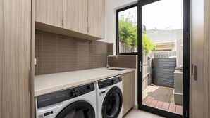 A compact laundry room with a washing machine, a sink, and a window leading to a backyard.