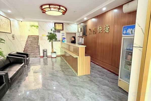 Zona de recepción de un hotel, con mostrador, escalera y refrigerador.