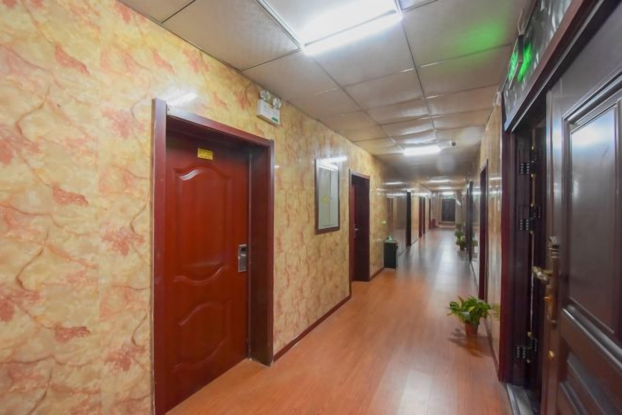 A hotel corridor with wooden flooring, marble walls, and doors leading to rooms.