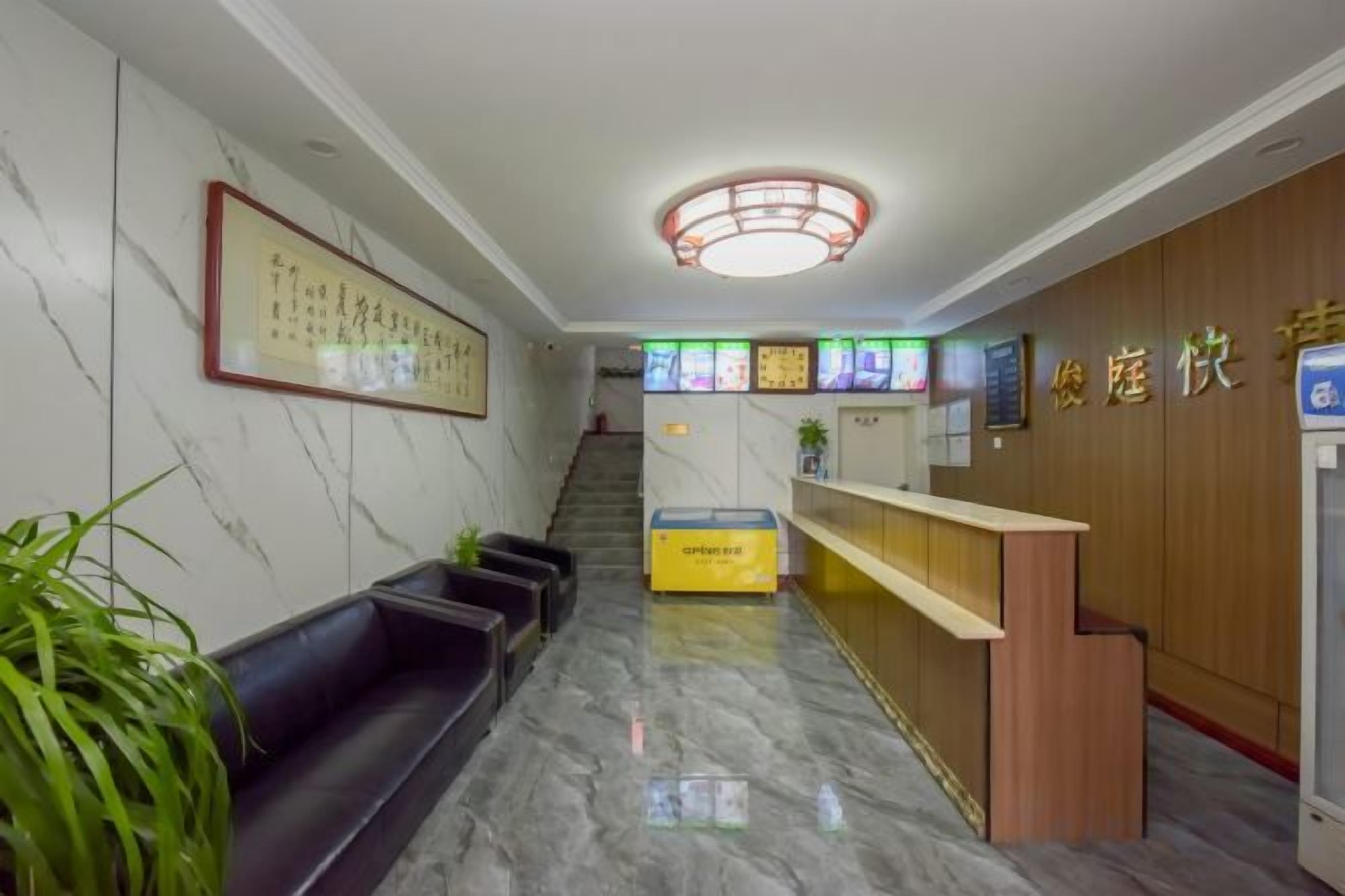 A hotel reception area with a marble floor, a reception desk, a staircase, and a framed artwork on the wall.