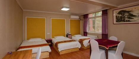 A hotel room with three single beds, a wooden table, white chairs, and a window with curtains.