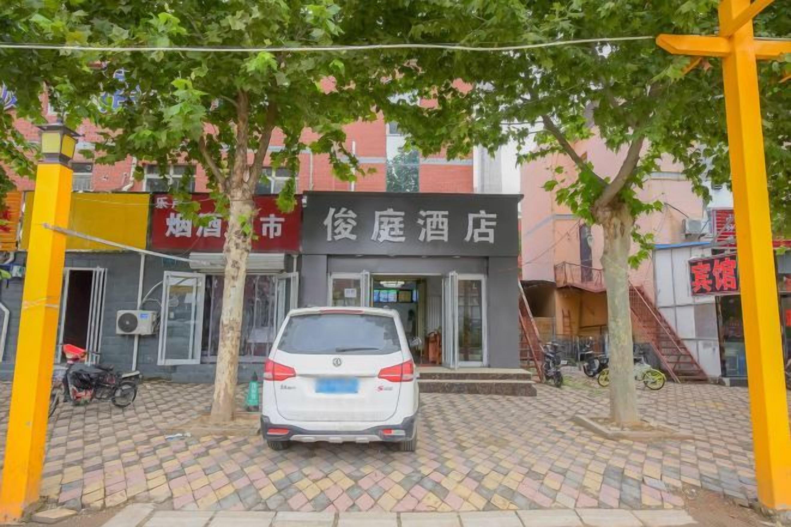 A hotel entrance with a car parked in front, a tree, and a building with signage.