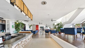 Eine großzügige Hotelhalle mit einer zentralen Sitzecke, einem Empfangsbereich und einer Treppe, die in eine obere Etage führt.