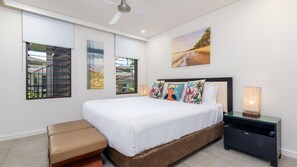 Une chambre à coucher moderne avec un grand lit, un banc, une table de chevet et des œuvres d’art accrochées aux murs.