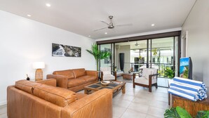 Una sala moderna con sofás de cuero, una mesa de centro y un televisor. Hay un balcón con vistas al exterior.
