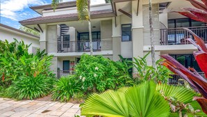 Un edificio de varios pisos con balcones, rodeado de exuberante vegetación y plantas tropicales.