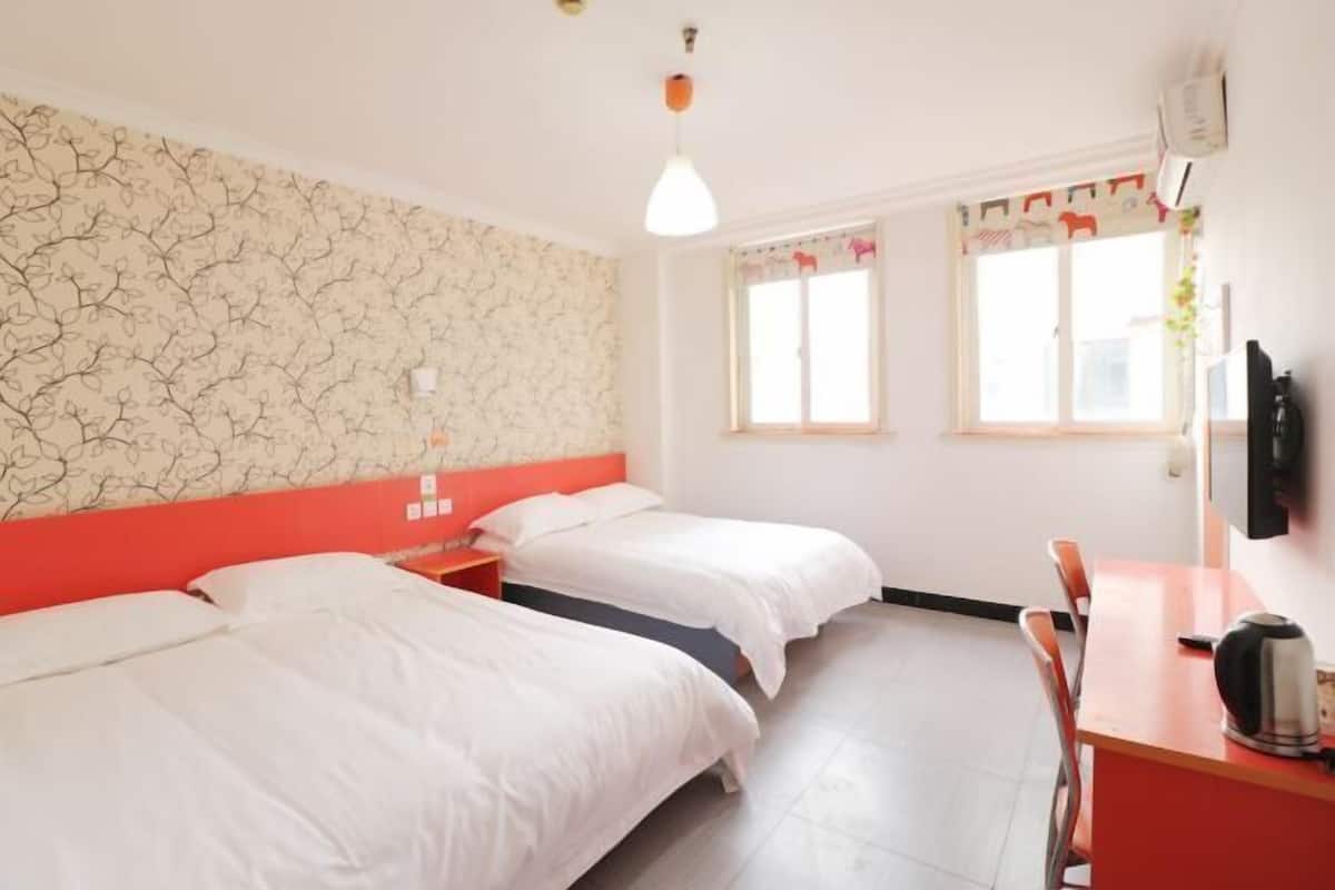 A hotel room with two beds, a desk, a chair, and a window.