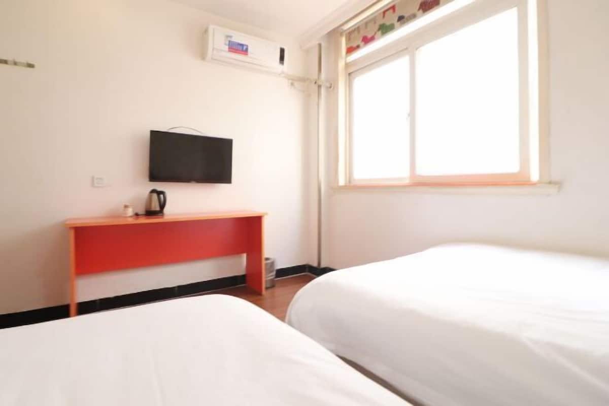 A hotel room with two beds, a red desk, a television, and a window.