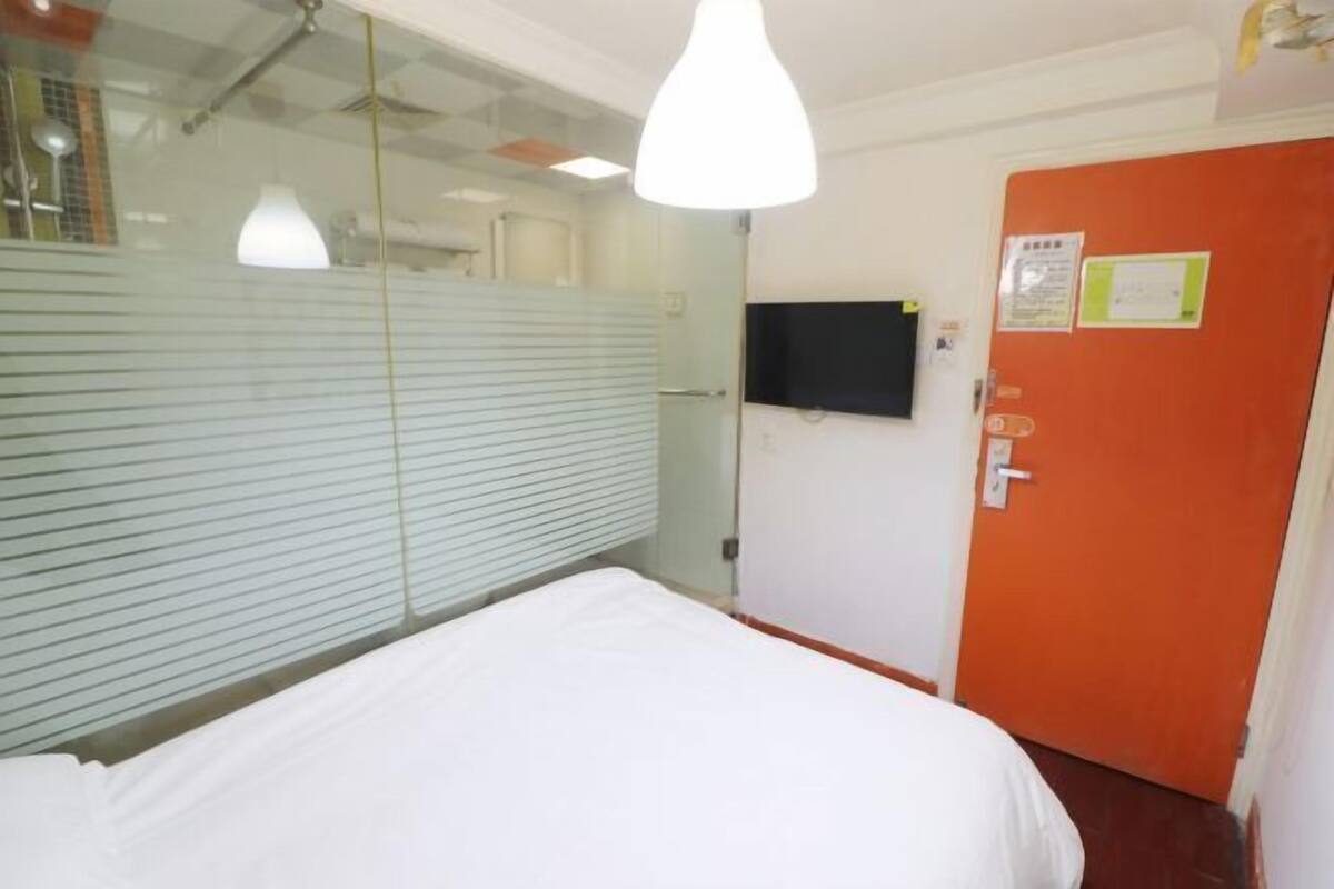 A room with a bed, a television on the wall, and a door with a sign.