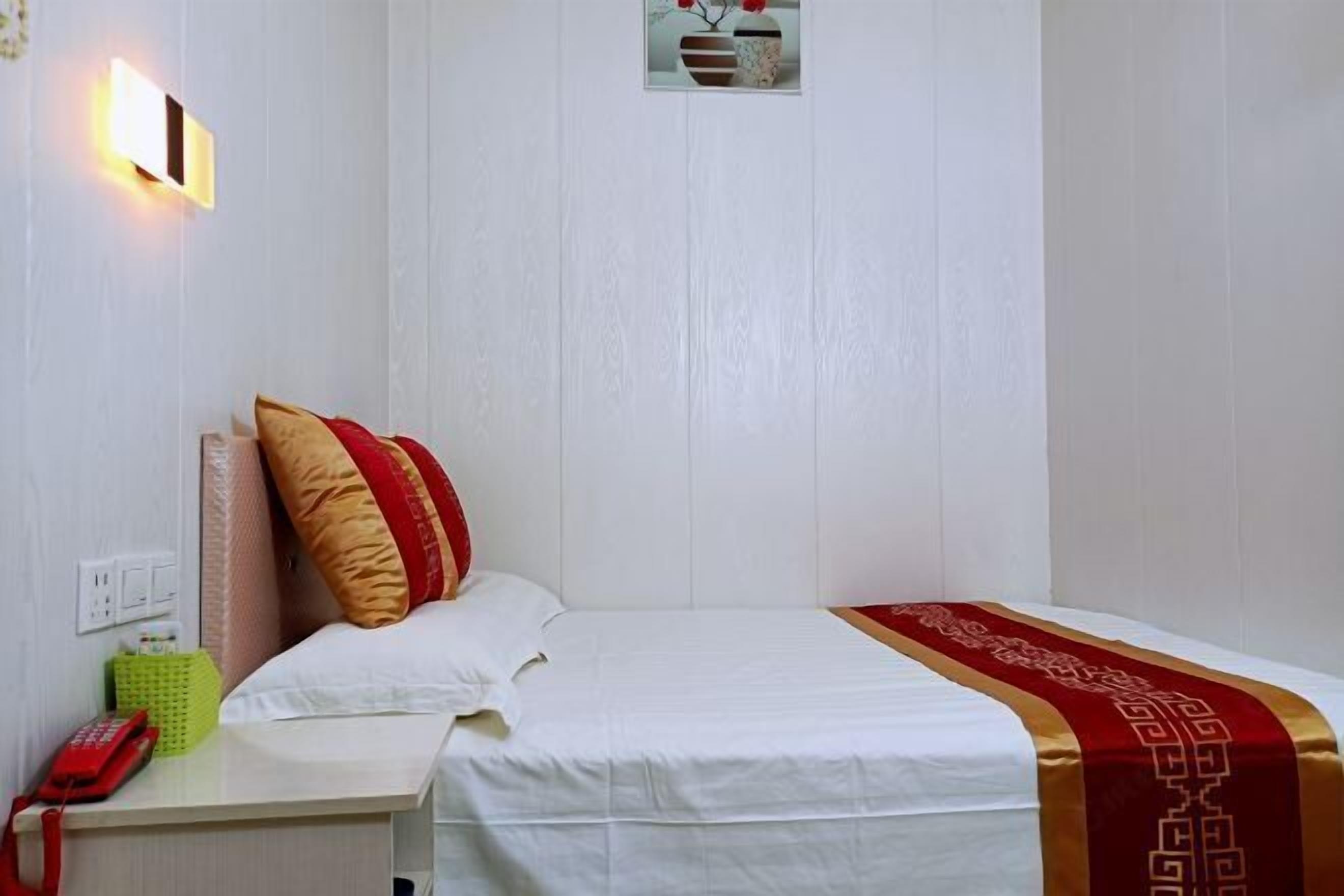 A hotel room with a bed, a bedside table with a telephone, and a wall-mounted light.