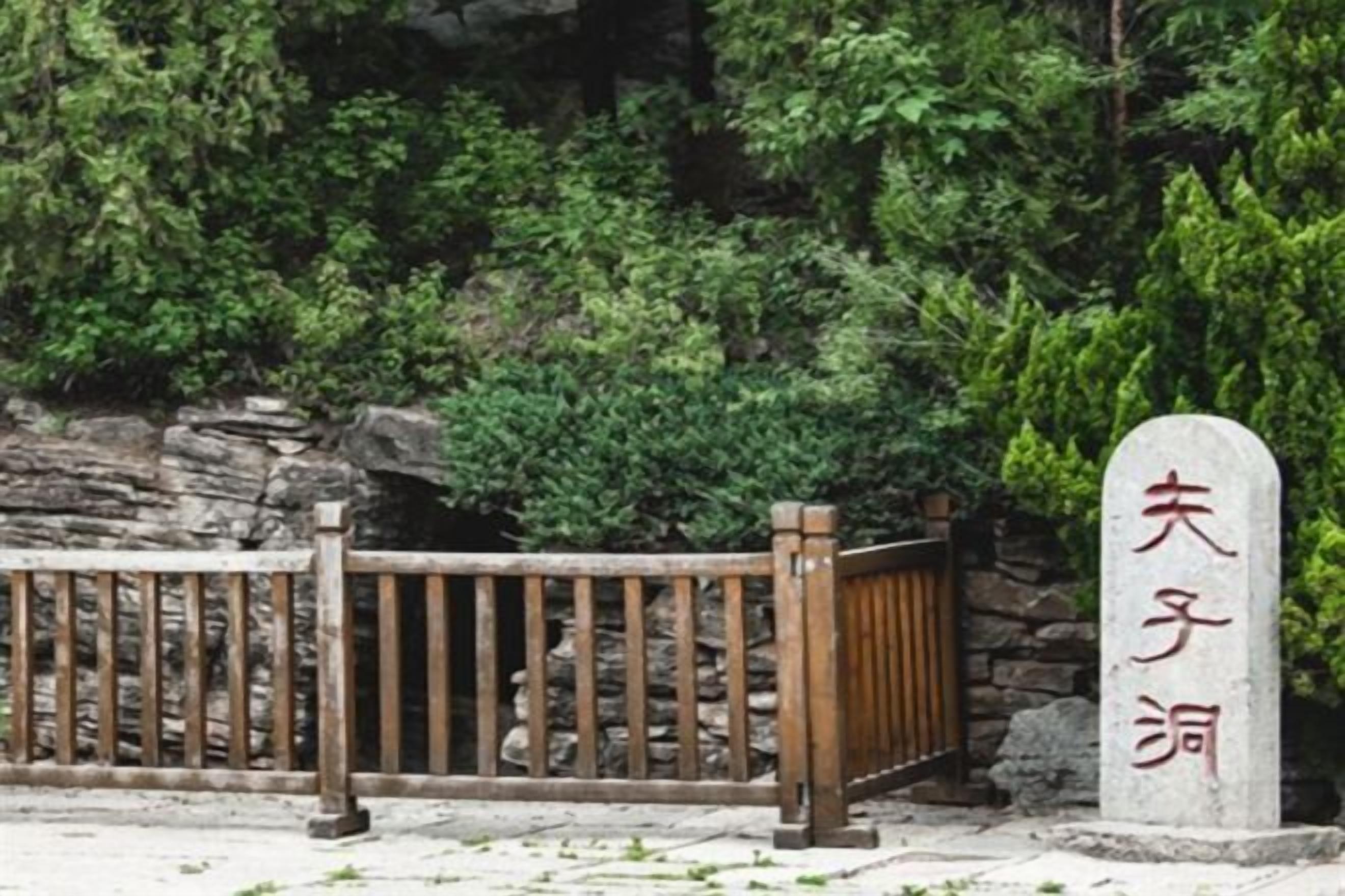 A stone monument with Chinese characters, a wooden fence, and a stone wall with greenery behind it.