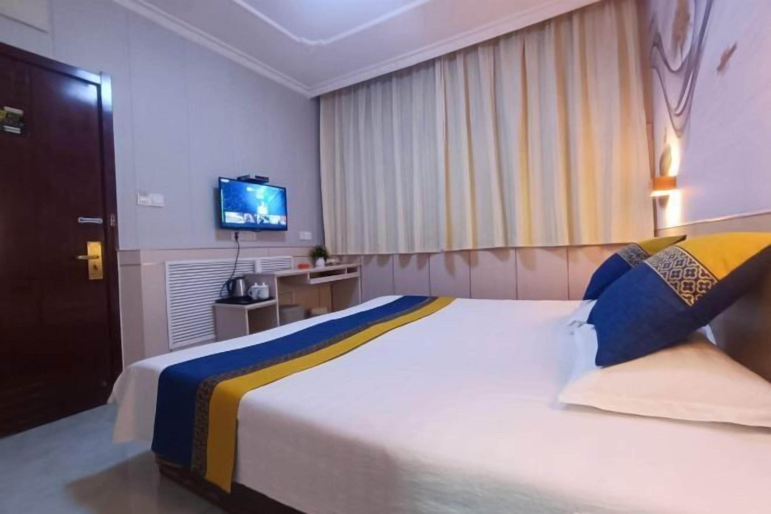 A hotel room with a bed, a television, a desk, and a window with curtains.