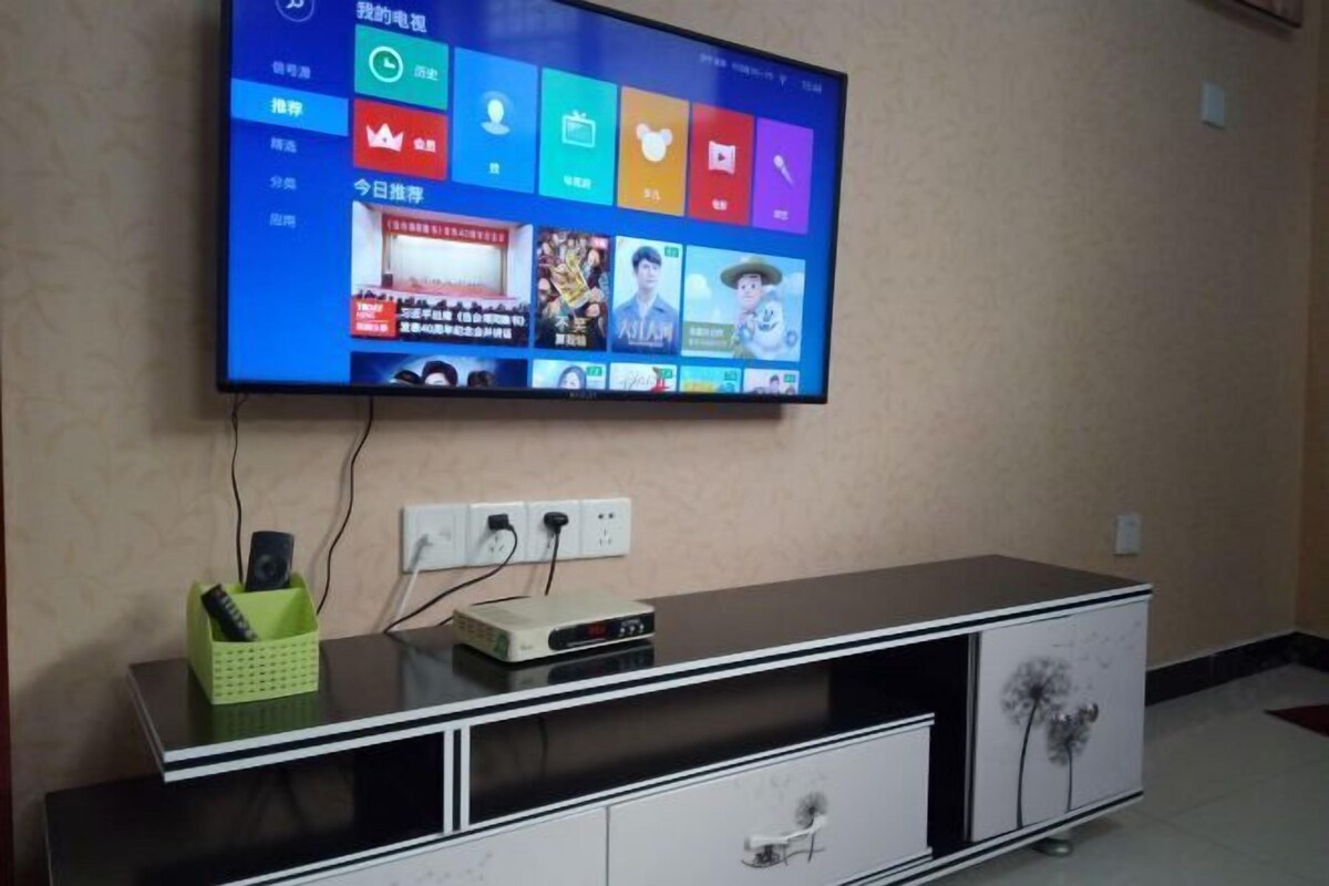 A flat-screen TV mounted on a wall above a black entertainment unit with a green remote holder and a DVD player.