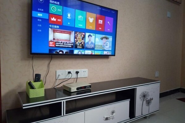 A flat-screen TV mounted on a wall above a black entertainment unit with a green remote holder and a DVD player. - Garden Hotel (Sankong Scenic Spot) (Qufu)
