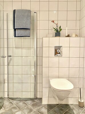 Bathroom features a glass shower enclosure, a toilet, and a potted plant.