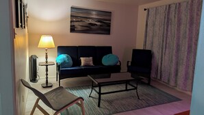 Una sala de estar con un sofá, una silla, una mesa de centro, una lámpara y un cuadro en la pared.