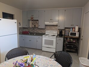 A compact kitchen with white cabinets, a stove, a microwave, and a small dining area with wicker chairs. -  3-bedroom Make yourself home while in  Rockdale B (Rockdale)