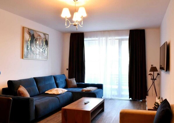 Een moderne woonkamer met een blauwe bank, een houten salontafel en een vloerlamp.